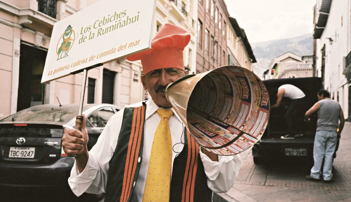 A street performer in Quito, Ecuador, promoting Los Cebiches de la Rumiñahui with a sign and megaphone.