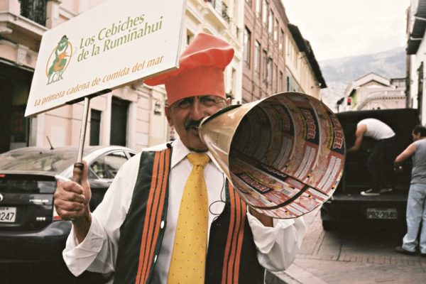 A street performer in Quito, Ecuador, promoting Los Cebiches de la Rumiñahui with a sign and megaphone.